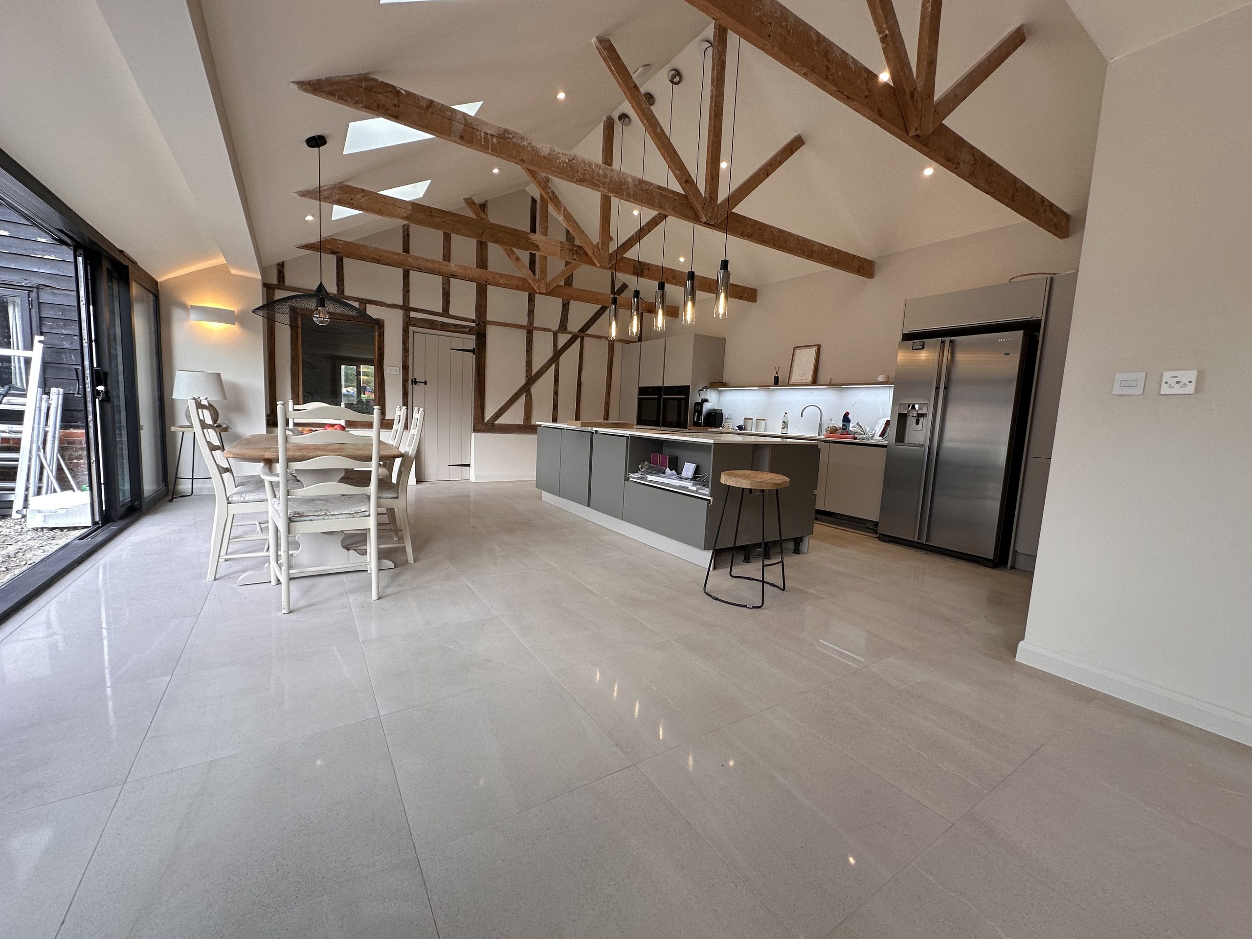 Open plan barn kitchen with a grey island, exposed oak trusses, vaulted ceiling and pendant lighting over a dining table