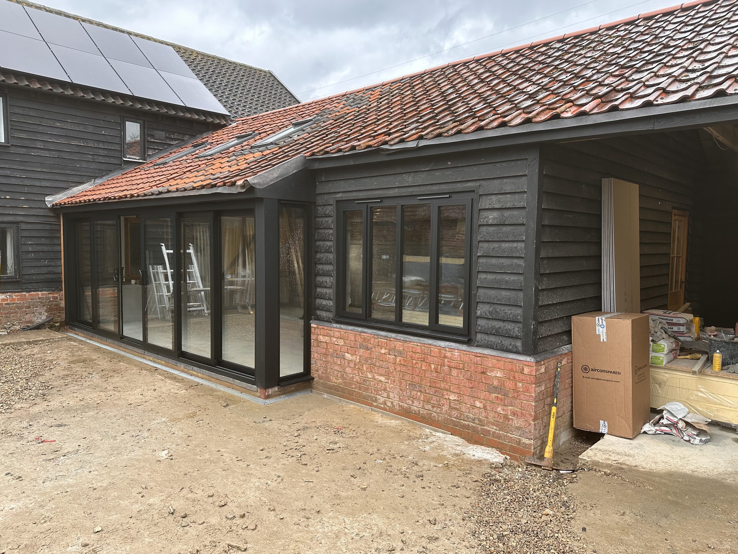 Newly built extension with black weatherboard cladding, a clay tiled roof, brick plinth and grey bifold doors