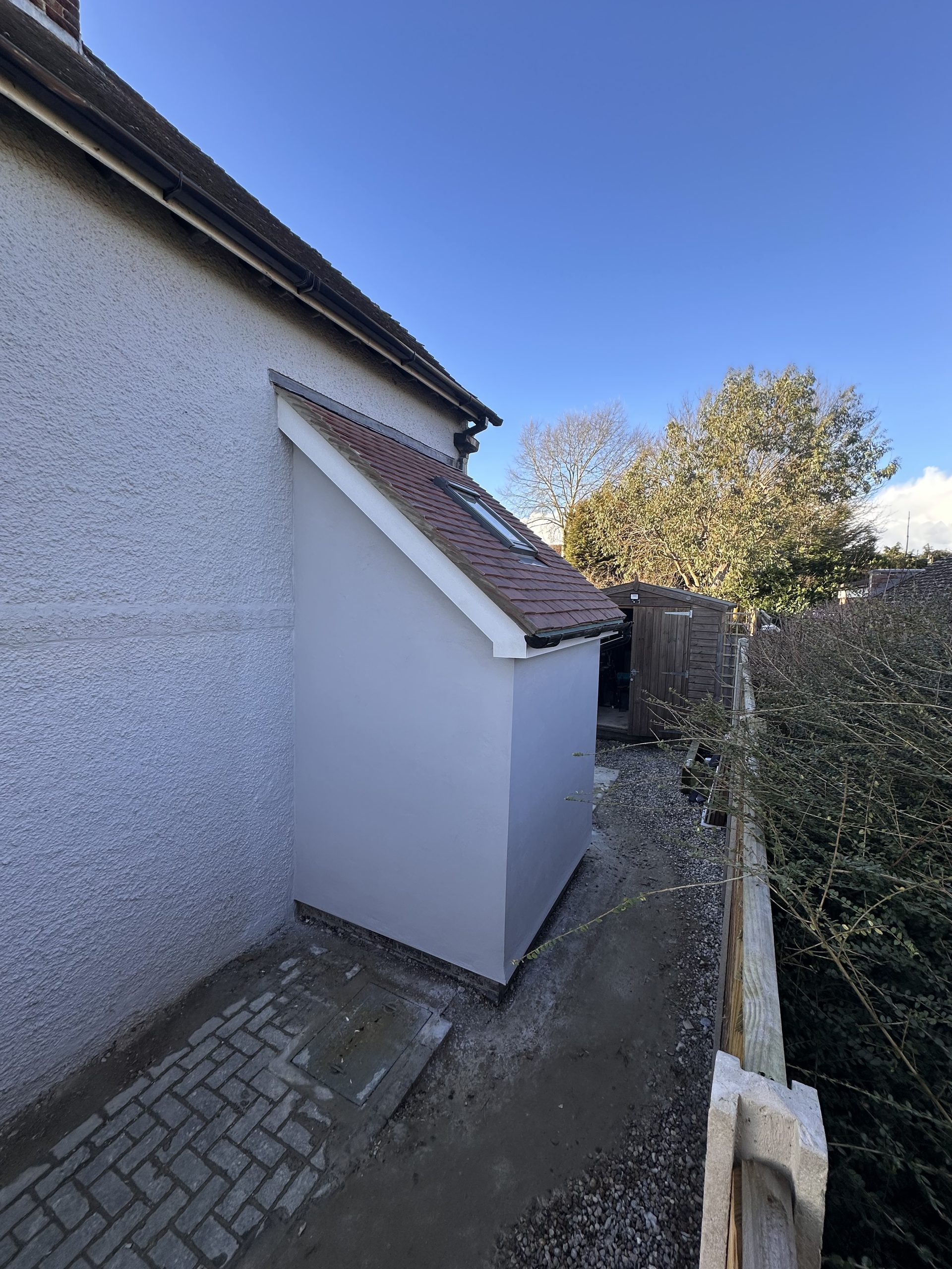 Newly built rendered side extension with a pitched tiled roof and roof window, finished with block paving